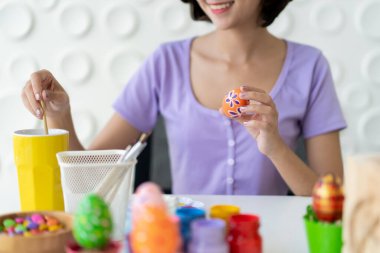Asyalı genç ve güzel bir kadın Paskalya yumurtası festivali için fantezi yumurtalarına su renkleri çizmeyi seviyor..