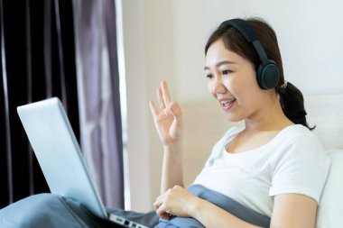 Ev konseptinde çalışan Asyalı genç bir kadının portresi. Mutlu Asyalı kadın evde kaldığı süre boyunca arkadaşıyla video konferansı yaparken 