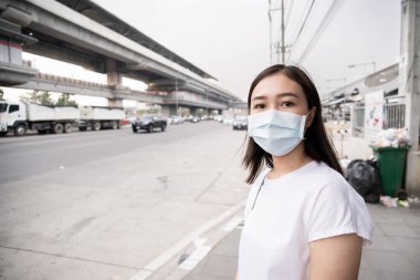 Kirli şehirde yolun kenarında duran Asyalı kadın tamamen PM2.5 tozuyla dolu. Kendini sis ve pm2.5 tozlu parçacıklardan korumak için koruyucu maske takan bir kadın. Çevre kirlilikten zarar gördü.