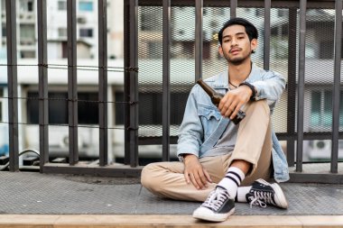 Umutsuz ve alkol bağımlısı işsiz Asyalı genç bir adam yolun kenarında bira şişesiyle tek başına oturuyor. Yaşam yetmezliği, depresyon, korku ve kriz sorunu kavramı. Kopyalama alanı olan fotoğraf.