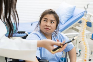 Asyalı şişman kadın hasta hastanedeki uzman doktorla sağlık hastalığı hakkında konuşuyor. Kadın omurgasındaki kritik sorun için endişeleniyor. Aşırı kilolu olması fiziksel yaralanmaya neden olabilir..