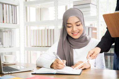 İki Asyalı Müslüman iş kadını ofiste konuşuyor ve birlikte çalışıyorlar. Çeşitlilik kültürel ve cinsiyet kavramı.