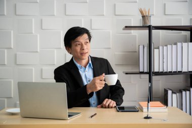 Asyalı yaşlı işadamının sabah ofiste portresi, iş yerinde kahve içen sıradan bir işadamı..