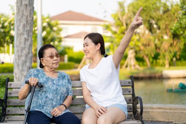 Torunu işaret parmağıyla gökyüzünü gösteriyor ve büyükannesinin bakmasına izin veriyor. Asyalı ailede mutlu bir ilişki. Emeklilikten sonra ailenin yaşlılarına bakmak.