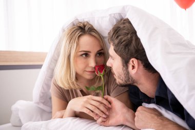 Genç Batılı çift yatak odasında romantik anlar yaşıyor. Adam sevgililer gününde karısına güzel kırmızı bir gül veriyor..