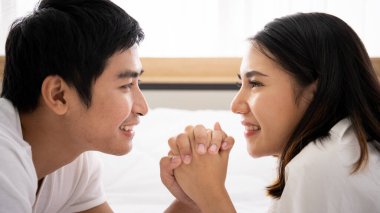 Yatak odasındaki komik ve romantik Asyalı çift portresi. Pencereden yansıyan doğal ışık, karı koca arasındaki ilişki ve aile olma kavramı..