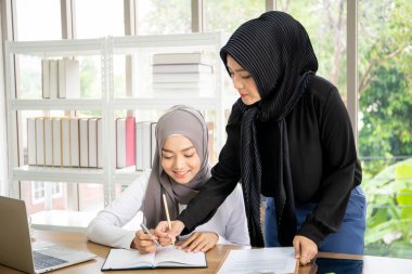 İki Asyalı Müslüman iş kadını ofiste konuşuyor ve birlikte çalışıyorlar. Çeşitlilik kültürel ve cinsiyet kavramı.