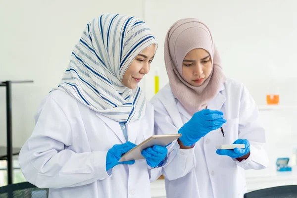化学実験室で実験をしている2人のアジア系イスラム教徒の科学者が — ストック写真