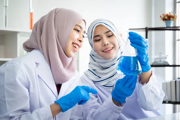 Happy Asian muslim scientist student investigating a chemistry together in laboratory. Two intelligence Muslim chemistry researcher examining and testing for pharmaceutical chemistry. Bio tech concept