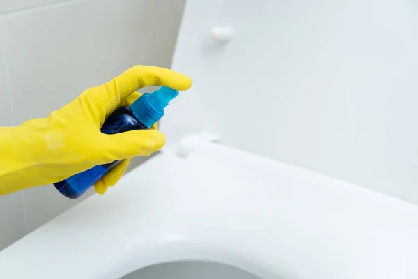 Housekeepers' hands in rubber protective grove while cleaning the dirty toilet. Maid spraying cleaning liquid solution, detergent on a flush toilet seat. Cleaning servant occupation