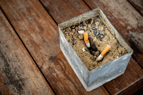 Dirty sand ashtray on the wooden table close up. Smoking and unhealthy behavior concept.