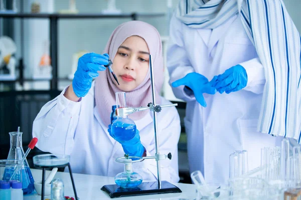 Happy Asian muslim scientist student investigating a chemistry together in laboratory. Two intelligence Muslim chemistry researcher examining and testing for pharmaceutical chemistry. Bio tech concept