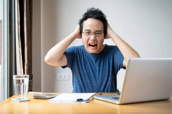 Young Asian businessman in relax casual during working from home. Asian man staying at home and setup a small workplace during COVID-19 self isolation. Work from home concept during coronavirus crisis