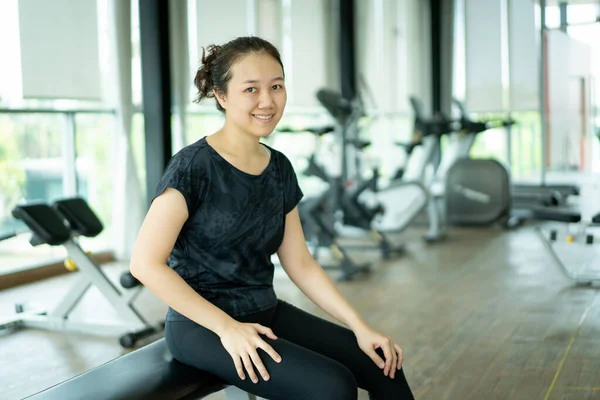 Spor salonunda ağırlık antrenmanı ve kardiyo egzersizinden sonra gülümseyen ve poz veren Asyalı güzel bir spor kadını. Spor salonunda vücut çalışan sağlıklı zayıf bir kadın, arka planda egzersiz makineleri.