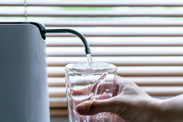 Man pouring water from the water purifier or water filter into a drinking glass close up. Water purification and making water purity before drinking. Healthcare in healthy people lifestyle concept.