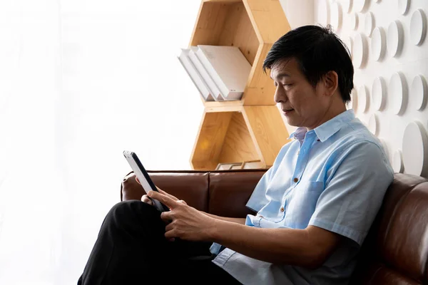 Handsome Asian elder man relaxing in living room, man using digital tablet.