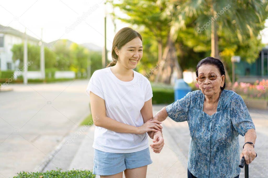 Granddaughter assist her grandmother whose age almost 90 years old exercise by walking at the park in the morning. Asian woman helping retired elder woman walking. Healthcare, wellness and wellbeing.