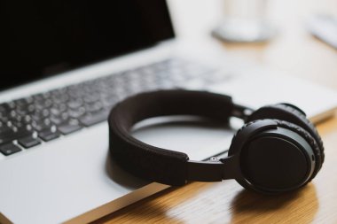 Laptop bilgisayarında sol tarafında fotokopi alanı olan kablosuz kulaklıklar bırakılmış. Ev ve ofis kavramından çalış. Çalışma saatinde rahatlama.