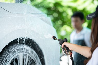 Garajda çalışan adam yüksek basınçlı köpük enjektörüyle kirli beyaz bir arabaya püskürtüyor. Yağmur mevsiminde araba yıkama ve araba bakım konsepti. El emeği kirli bir arabaya sıvı sabun püskürtür..