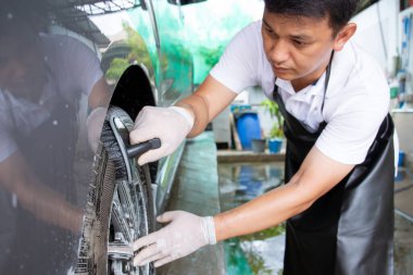 Araba bakım garajında Asyalı işçiler kirli araç tekerlerini fırça ve sıvı sabun köpüğü kullanarak temizliyor. Araba bakımı konseptinde çalışan yetenekli Asyalı işçiler.