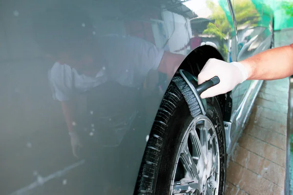 Asian worker in car care garage cleaning a dirty vehicle wheels by using brush and liquid soap foam close up with copyspace. Skilled Asian labor working in car care service concept.