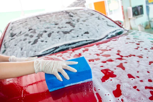 Neşeli, güzel Asyalı kadın modern kırmızı arabasını yüksek basınçlı su ve araba yıkama süngeri kullanarak yıkıyor. Garajda fotokopi makinesiyle araba yıkarken kameraya bakan genç bir kadın..