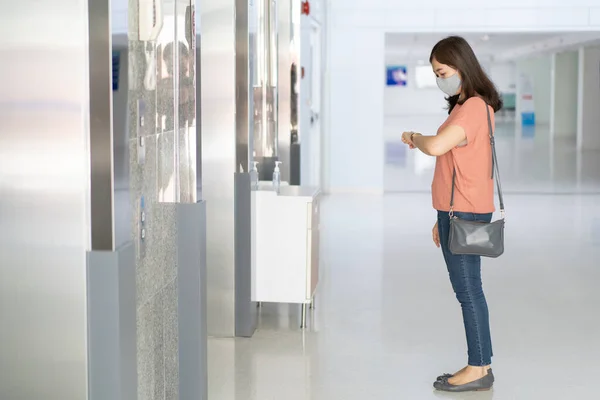 Woman standing and waiting for the elevator in the building, woman looking at her watch while waiting the elevator.