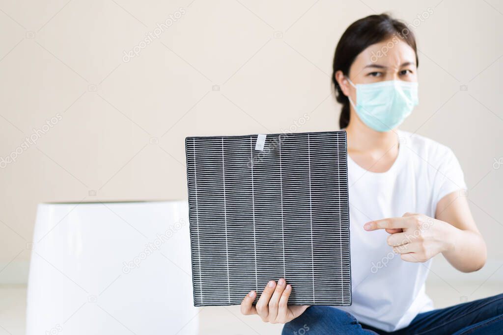 Asian woman wearing a hygiene protective face mask during changing a dirty air filter in the air purifier machine close up with copyspace. Hygienic lifestyle and prevention from illness concept.