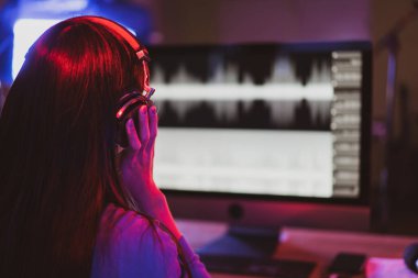 Güzel Asyalı ses mühendisi stüdyoda dijital ses kaydıyla çalışıyor. Kadın ses mühendisi bilgisayar ekranındaki ses dalgasına bakarak şarkıcının şarkısını ve sesini kaydediyor..