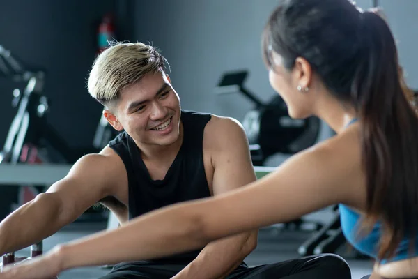 Two Asian sportsman and sportswoman doing a leg stretching together before exercise. Young adult people workout together in a fitness gym close up, work life balance concept. Exercise motivation.