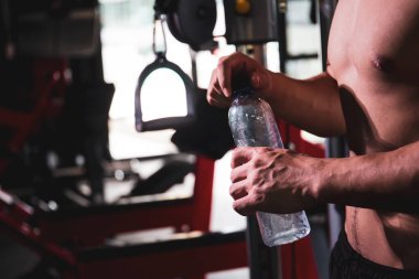 Spor salonunda egzersiz yaptıktan sonra su şişesinden su içen güçlü bir sporcu. Üstsüz sporcular idmandan sonra soğuk su içerek kendilerini tazelerler. Kopyalama alanı olan resim.