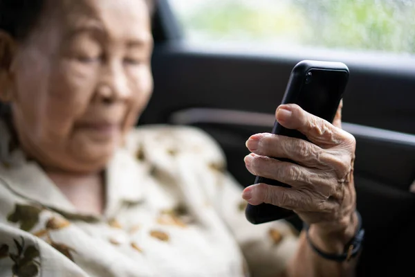 Very old Asian passenger woman age between 80 - 90 years old traveling by the car while raining and using a video call. Cheerful retired woman in a private car portrait with copy space.