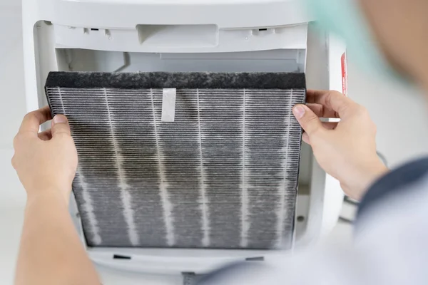 Asian woman changing the dirty air purifier filter after using for a long time in the dirty air environment. Using air purifier clean the air for better atmosphere in a house.