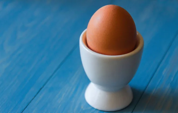 Boiled egg in a white egg cup, on a wooden blue background