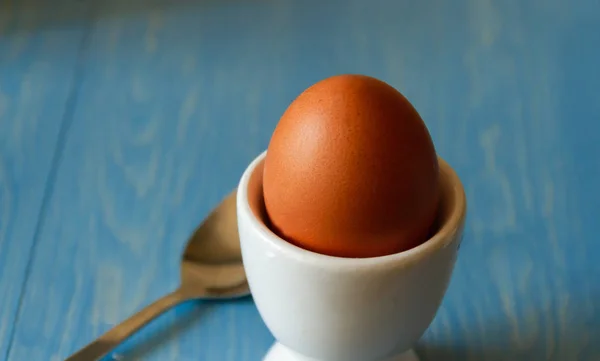 Boiled egg in a white egg cup with spoon on a blue background