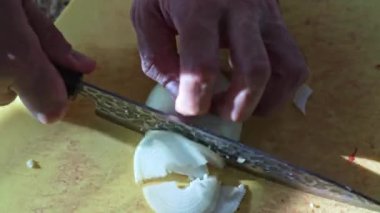 Kapalı eller mutfak masasında soğanı yarım halkalara bölüyor, bıçakla doğranmış sebze, taze malzeme hazırlığı, ev yapımı pişirme süreci, otantik mutfak yemeği 4K görüntüleri.