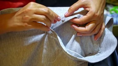 Çocuk polo tişörtüne iğne iplik iliştirilmiş dikiş düğmesi, Bokeh ile seçici odak, otantik ev kıyafetleri tamiri, günlük ev işi 4K video görüntüleri