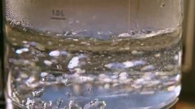 Closeup shot of boiling water inside a glass kettle recorded in real time with selective focus and visible bubbles and steam.
