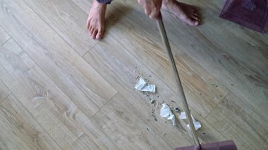 Medium shot lower body view of person sweeping trash on wooden floor with broom and collecting into dustpan at home, casual domestic cleaning process, everyday housekeeping 4K video footage