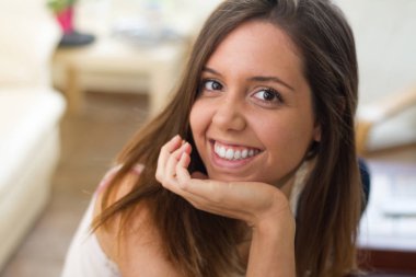 Çenesindeki eliyle evinin oturma odasında güçlenmiş mükemmel bir gülümseme mutlu mutlu ve kendine güvenen genç esmer kadın,