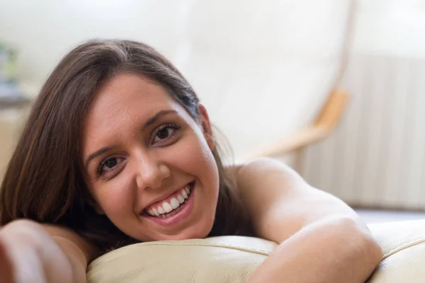 Perfect smile European brunette woman with brown eyes and sweet features lying on the sofa with the side face happy and smiling towards the viewer