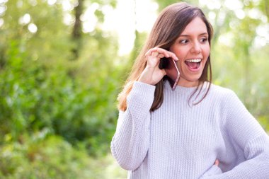 Güzel genç esmer kadın cep telefon Dedikoducu ağaç arka plan ile doğada dinlerken çok mutlu ederken