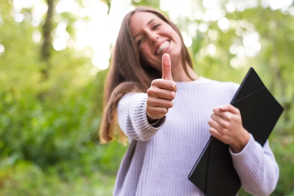 Female or young Caucasian european college girl or student with folder in college after doing final exam and refresher classes with thumps up smile and happy