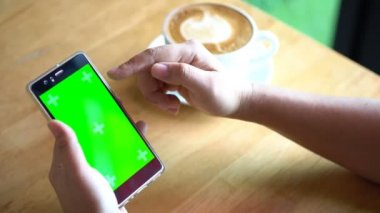 Smartphone cep telefonu ile chroma anahtar yeşil ekran. Çalışma ya da kahve dükkanı, bir yandan beyaz kafe geç Kupası tutarak ve içme ve başka bir el cep telefonu, 4 k görüntüleri tutarak smartphone kullanarak kadın