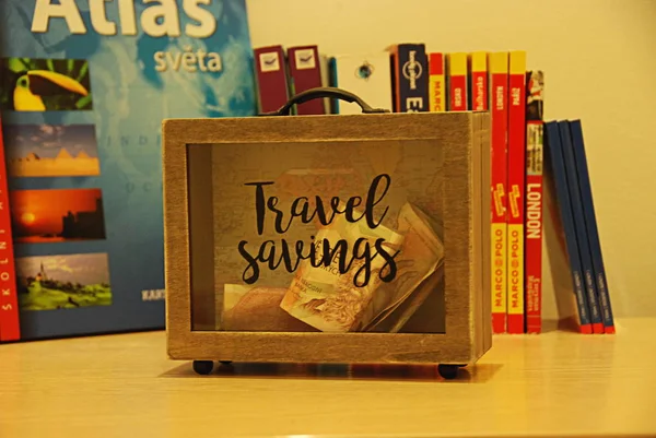 木製のスーツケース形のお金箱 ブックガイドの背景で旅行のお金の節約 — ストック写真
