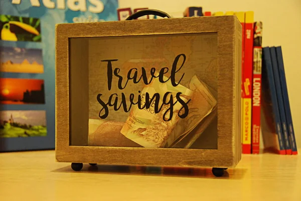 旅行の節約で形作られたスーツケースのマネーボックス 背景にブックガイド — ストック写真