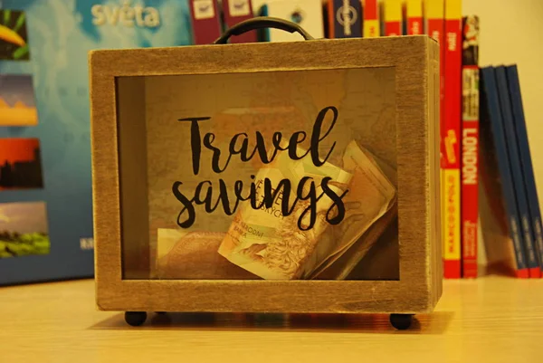 木製のスーツケース形のお金箱 ブックガイドの背景で旅行のお金の節約 — ストック写真