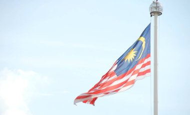 Arka planda açık mavi gökyüzü ile rüzgarda sallayarak bayrak direğinde Malezya bayrağı