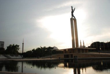 Istiqual Camii kubbesi ile Jakarta Lapangan Banteng Parkı Irian Jaya Kurtuluş Anıtı üzerinde bir gün batımı, dalları ile görünümü