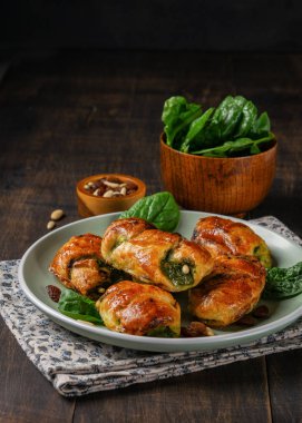 Mini ıspanak kruvasan kuru üzüm, pinyonlar ve keçi peyniri ve ıspanak koyu arka plan ile plaka üzerinde bir kase ile. Metin, dikey için yer. Sağlıklı kavramı.